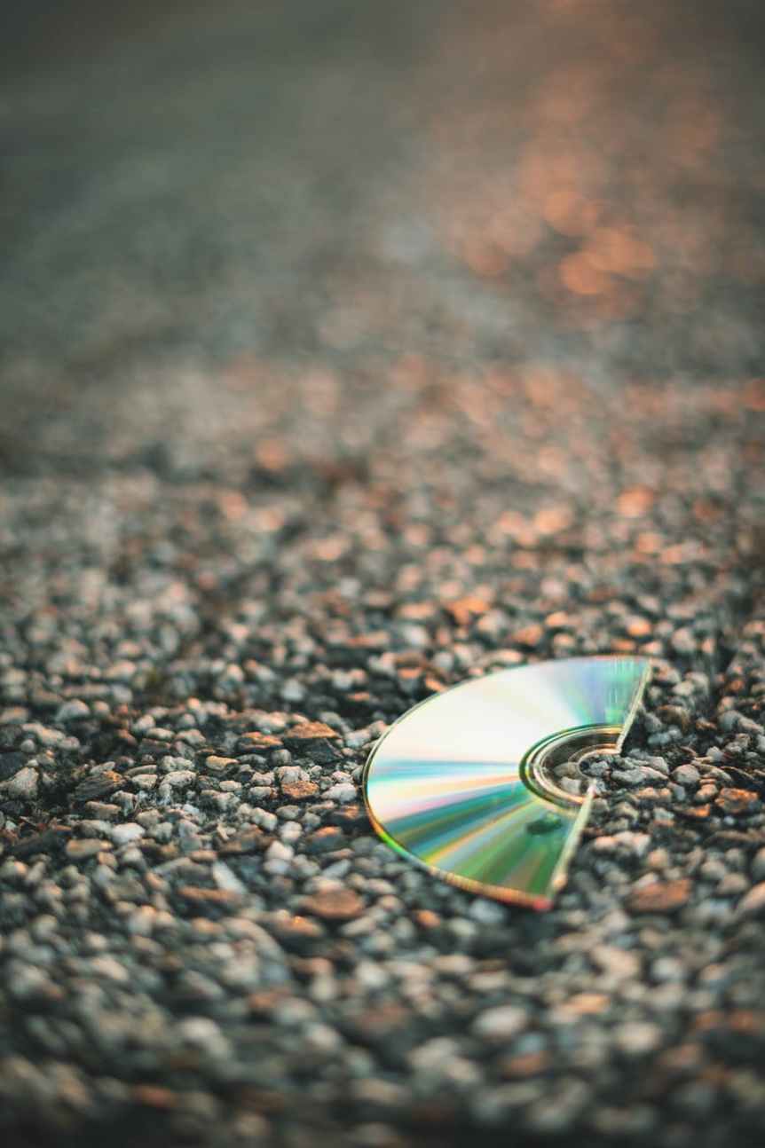 selective focus photography of half cut compact disc on gray pavement